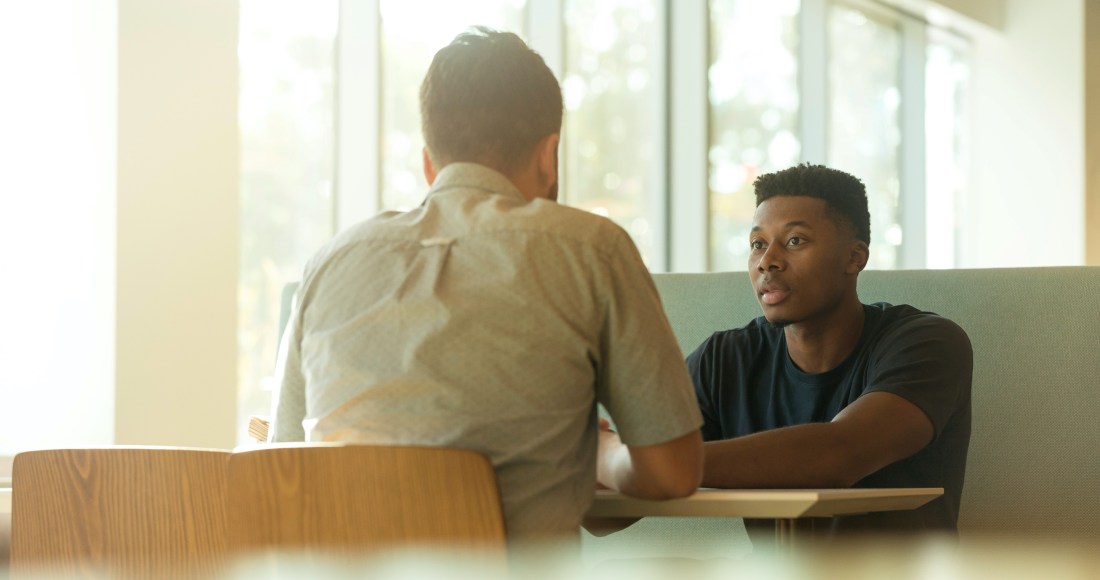 Two men sit at a table facing each other