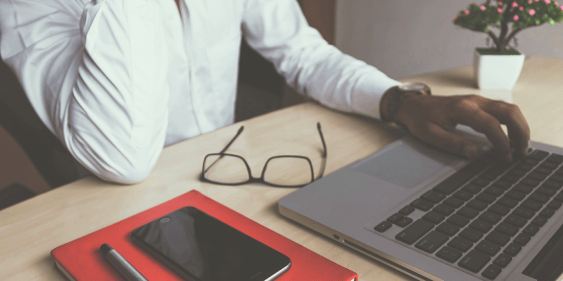 Person sitting at a table with their hand on their laptop